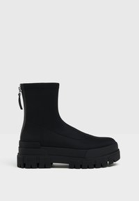 Black ankle boots made of smooth material with a chunky sole, featuring a rear zipper and minimalist design for streamlined appearance.