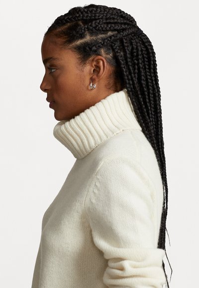 Cream-colored knitted sweater with a tall, ribbed turtleneck. Features long sleeves and textured fabric, highlighting a relaxed fit.