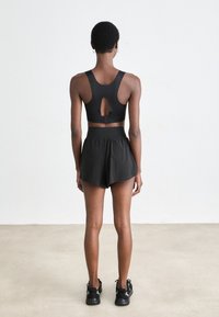 Reggiseno sportivo nero con schienale a occhiello, abbinato a pantaloni corto neri. Tessuto liscio, design minimale e spalline di supporto. Scarpe da ginnastica nere.