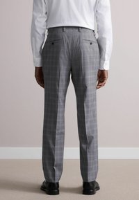 Pantalons gris à carreaux avec une coupe ajustée, fabriqués en tissu lisse. Comprend deux poches arrière et un design à plis à l'avant. Chaussures noires visibles.