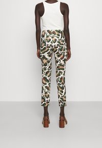 Pantalons ajustés blancs avec un motif abstrait vert, marron et noir. Tissu lisse au toucher ; longueur cropped et taille haute.