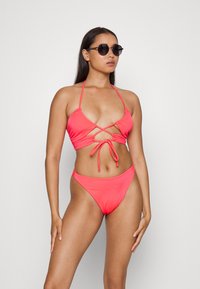 Conjunto de biquíni rosa com decote halter e design entrelaçado. Tecido suave com parte de baixo de cintura alta a condizer. Óculos de sol usados.