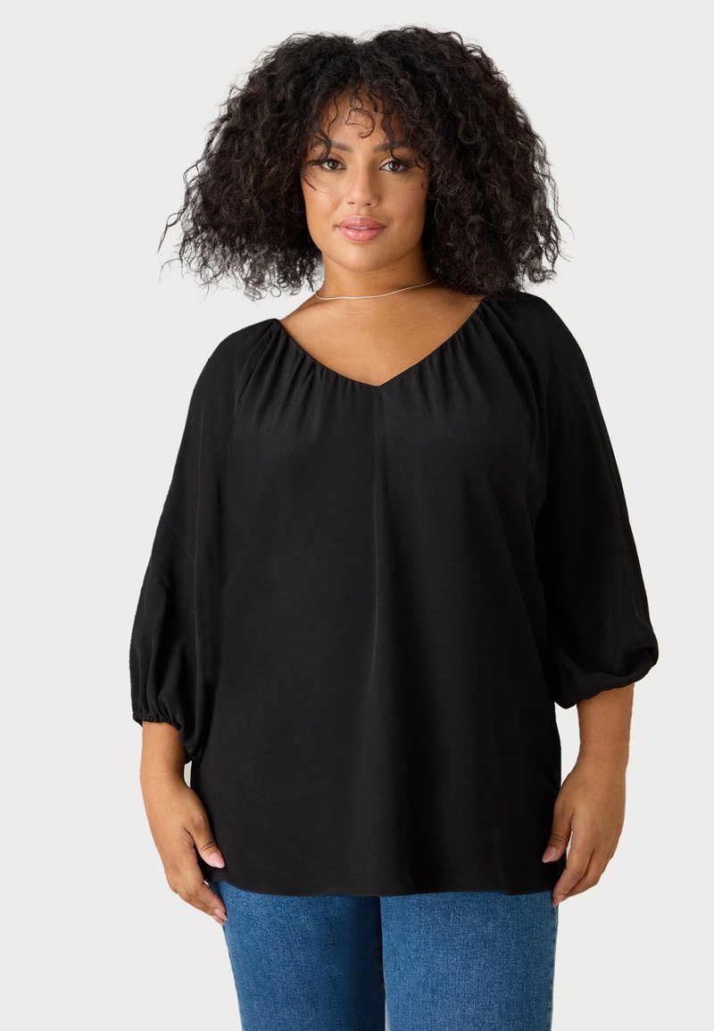 Blusa nera con scollo a V e dettagli arricciati sulle spalle, maniche puff a 3/4. Tessuto morbido con vestibilità rilassata, abbinata a denim blu.