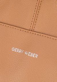 Texture in pelle marrone con grana visibile; presenta il logo "Gerry Weber" in rilievo e in argento. Il dettaglio delle cuciture aggiunge profondità alla superficie.