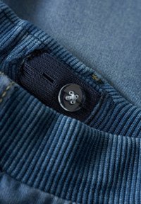 Denim oblačilo z rebrastim mornarsko modrim ovratnikom, prozornim gumbom pri odprtju in kontrastnim šivom ob robu ovratnika.