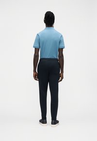 Blå poloskjorte med kortermet, kombinert med svarte joggebukser. Antrekket har en avslappet passform og er laget av mykt, glatt stoff.