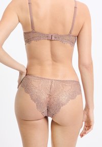 Reggiseno in pizzo e perizoma abbinato in malva con bordi smerlati. Motivi floreali delicati e spalline regolabili visibili. Materiale morbido e texturizzato.