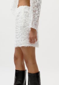Robe blanche avec une finition texturée semblable à des plumes, ourlet court et manches longues. Des bottes noires jusqu'au genou complètent la tenue.