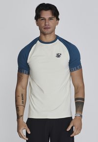 Raglan T-shirt in crème en marine, met korte mouwen, een ronde halslijn, zachte stof en een klein logo op de borst.
