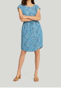 Blå blommig klänning med korta ärmar, insnörd midja och lös passform. Har ett subtilt mönster med nyanser av blått, grönt och rosa.
