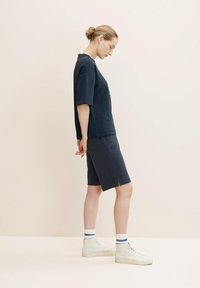 Navy cotton T-shirt and matching shorts, relaxed fit. White high-top sneakers with blue-accented socks. Minimalist design, smooth texture.