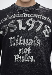 Pull noir avec texte blanc délavé disant "Rituals not Rules" et "SL978" en grandes lettres à l'avant.