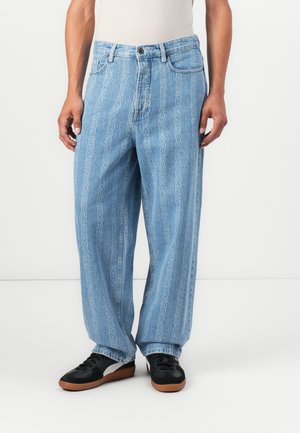Lichtblauwe denim broek met een kettingpatroon ontwerp, wijde pijpen, en vijf zakken, gecombineerd met zwarte sneakers.