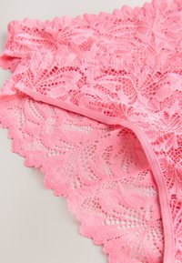 Tissu en dentelle rose avec motifs floraux et bords festonnés, montrant des détails en gros plan de la texture et des coutures.