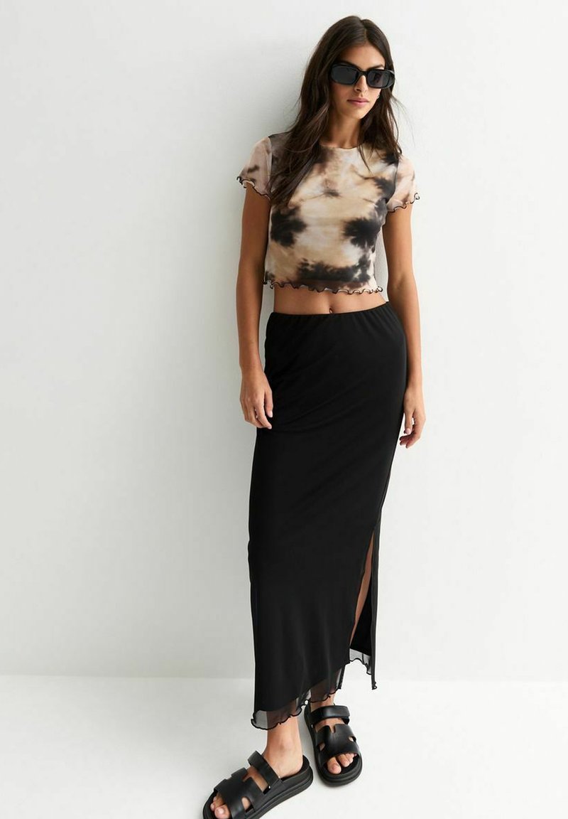 Korte tie-dye top in beige en bruin, met gerafelde randen; zwarte maxi rok met een zijsplit; chunky zwarte sandaal.