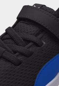 Μαύρο αθλητικό παπούτσι με υφασμάτινη υφή, μαύρα κορδόνια, μαύρο λουράκι με βέλκρο και μπλε πινελιά κοντά στη σόλα.