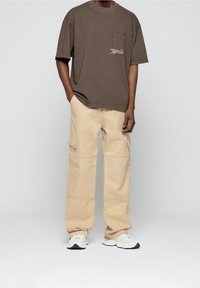 Brun oversized t-shirt med framficka. Beige cargo byxor med sidofickor och synlig sömnad. Vita sneakers med detaljer.