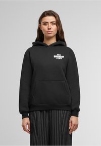 Black hoodie made from soft material, featuring a front pocket and a drawstring hood. "THE BRUNCH CLUB" is printed in white on the chest.