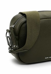 Borsa in pelle verde oliva con superficie strutturata, chiusura con zip e tracolla in tessuto; presenta dettagli in metallo argentato e logo.
