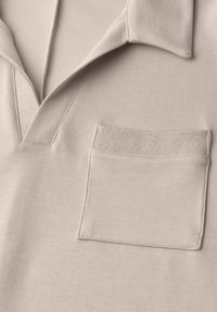 Polo beige en coton avec col ouvert et poche poitrine rectangulaire aux bords surpiqués.