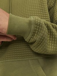 Olive green sweatshirt with a quilted texture, featuring ribbed cuffs. The design includes a smooth bottom section and fitted sleeves.