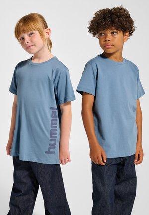 Två barn bär matchande blå kortärmade t-shirts med en "hummel"-grafik i mörklila på sidan, kombinerade med mörka denimjeans.