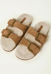 Braune Wildleder-Sandalen mit zwei verstellbaren Schnallen, weichem cremefarbenem Fleece-Futter, runder Zehenform und flacher Sohle. Minimalistisches Design mit praktischen Details.