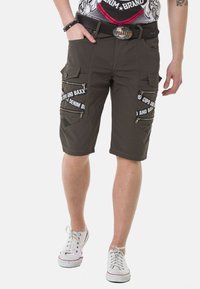 Dunkelolivfarbene Cargo-Shorts mit mehreren Reißverschluss- und Klappentaschen, mit weißem Logodruck. Hergestellt aus leichtem Stoff, knielange Schnittform.