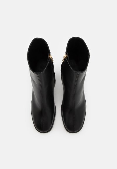 Bottes de cheville en cuir noir avec une texture lisse, un design épuré et des fermetures éclair en métal doré de chaque côté.