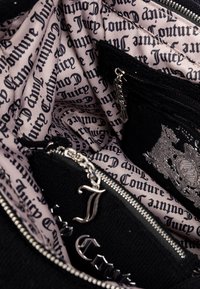 Interno di una borsa nera con foderatura rosa chiaro caratterizzata da ripetute scritte "Juicy Couture". Presenti elementi in metallo argentato e zip decorative.