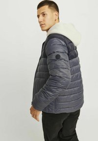 Chaqueta de plumas Navy con diseño de acolchado horizontal, sudadera con capucha sin detalles debajo y un parche redondo en la manga izquierda.
