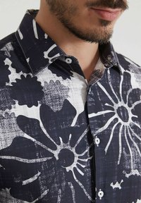 Chemise florale bleu marine avec des motifs blancs audacieux, un col boutonné et un tissu texturé avec un motif de grille subtil.