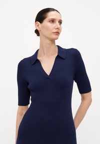 Robe côtelée navy avec des manches courtes et un décolleté en V. Présente un design à col et une silhouette ajustée. Texture lisse.