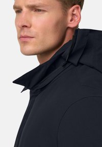 Črna zunanja oblačila z visokim ovratnikom, ki imajo zadrgo in gladko teksturo. Podrobnosti okoli ovratnika izboljšajo oblikovanje.