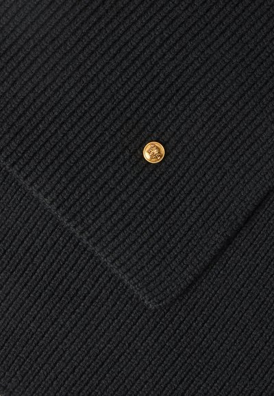Gros plan sur un tissu tricoté côtelé noir avec un petit bouton rond doré embossé d'un motif de visage au centre.