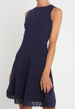 Robe bleu marine sans manches avec corsage ajusté et jupe évasée, avec une bordure en dentelle le long de l'ourlet.