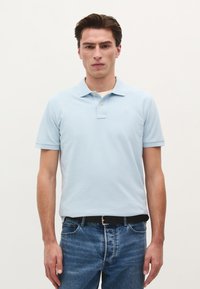 Lyseblå polo shirt med klassisk krave, korte ærmer og to knapper. Bæres med mørkeblå jeans og et sort bælte.