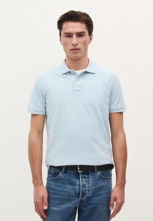 Lichtblauwe polo met een klassieke kraag, korte mouwen en twee knopen. Draag het met donkerblauwe spijkerbroek en een zwarte riem.
