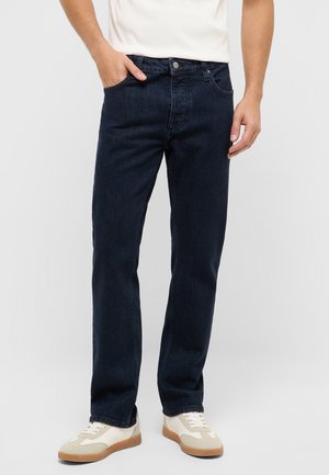 Dark blue denim jeans with a straight leg fit, featuring front pockets and a single button closure, paired with beige and white sneakers.