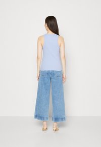 Světle modrý top bez rukávů s přiléhavým střihem, kombinovaný s širokými světle modrými denimovými džíny. Minimalistický styl s čistými liniemi a bez ozdob.