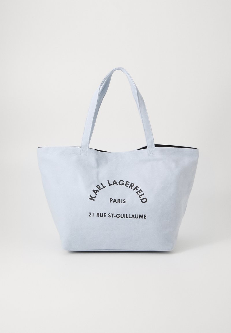 Sac fourre-tout en toile bleu clair avec un intérieur noir. Présente un texte noir audacieux : "KARL LAGERFELD PARIS 21 RUE ST-GUILLAUME." Poignées doubles robustes.