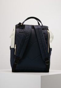 Granatowy plecak z tkaniny z białymi akcentami, regulowanymi paskami, złotymi zamkami błyskawicznymi oraz pikowanym wzorem z tyłu, który dodaje faktury i stylu.