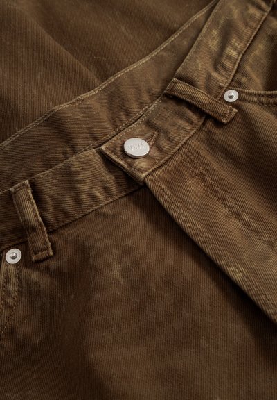 Brown corduroy fabric with visible ribbing, featuring a metal button and flat front pockets. Stitching detail is present along the waistband.