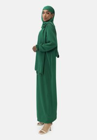 Grön lång klänning med en svängig silhuett, kompletterad med en matchande hijab. Tyget ser jämnt ut med en rik, djärv färg.