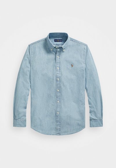 Light blue denim button-up shirt with long sleeves, collar, and front buttons. Features a small embroidered logo on the chest.