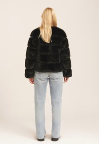 Black faux fur jacket with horizontal stripes, featuring a high collar and long sleeves. Paired with light blue denim pants.