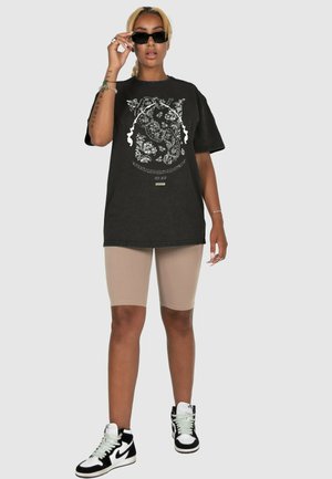 Schwarzes, übergroßes T-Shirt mit weißem Blumen-Grafikdesign, kombiniert mit beigen Radshorts und schwarz-weißen High-Top-Sneakers.