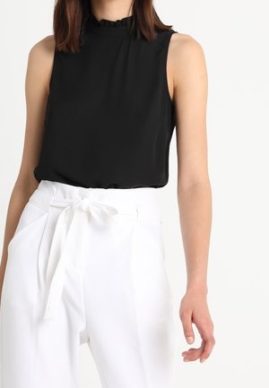 Top nero senza maniche con colletto arricciato, abbinato a pantaloni bianchi a vita alta con cintura legata e tasche laterali.