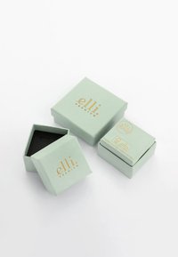 Myntegrønne dobbeltlagkasser med guldbogstaver. En kasse er åben og viser et sort indre. Simpel, geometrisk design.