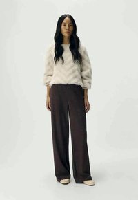 White, fuzzy sweater with puff sleeves paired with dark brown, wide-leg trousers. The outfit is completed with light-colored slip-on shoes.